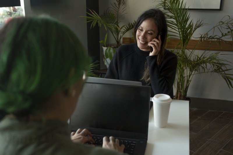 On a call while friend does work on a computer at a café
